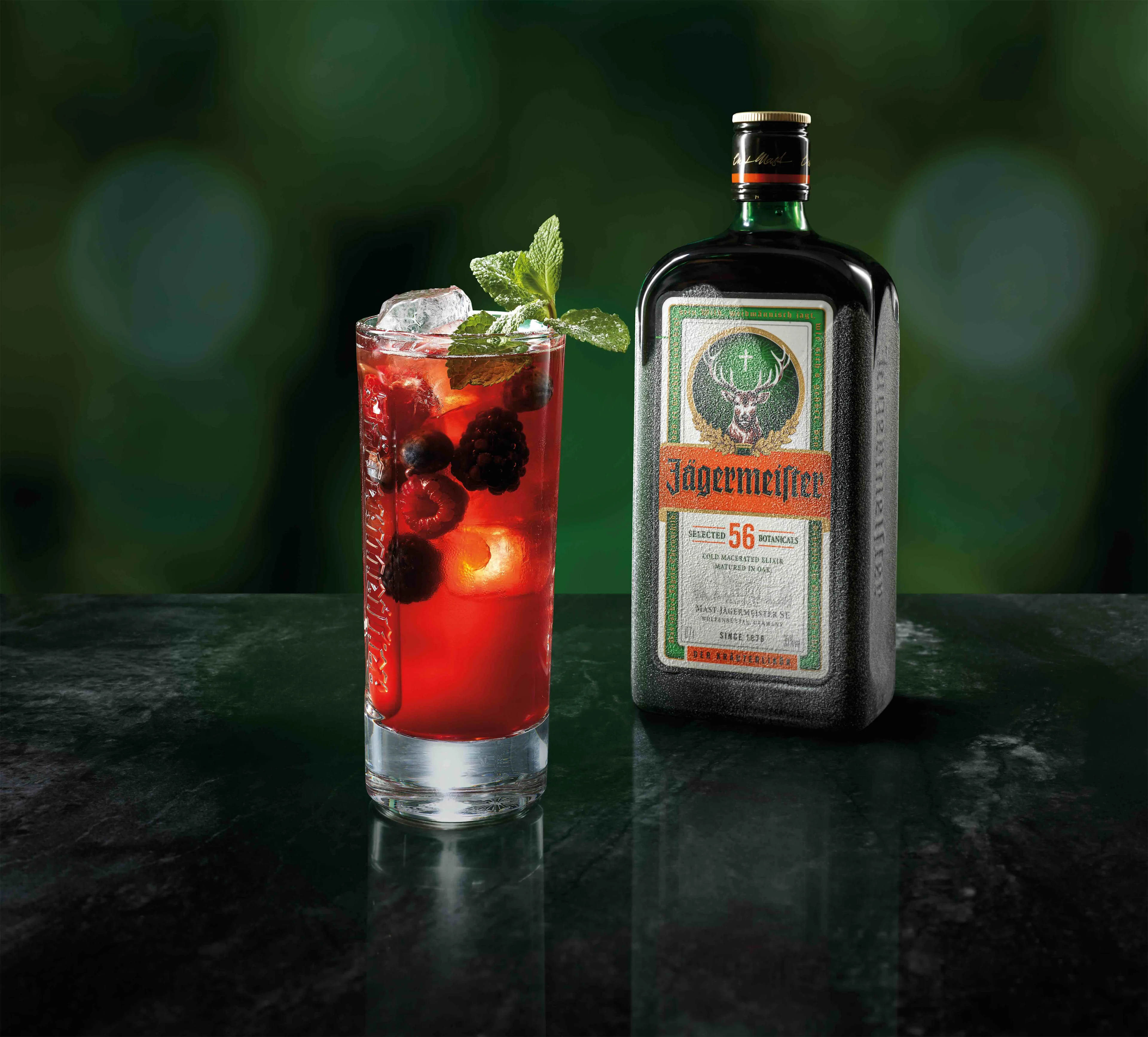 A glass of Jägermeister Purple Night in front of a Jägermeister bottle