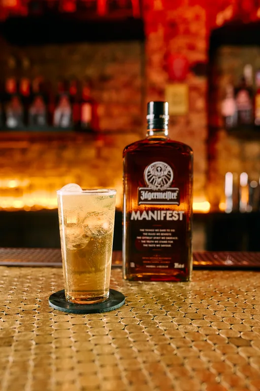 A glass of Manifest Ginger Ale in front of a Jägermeister bottle